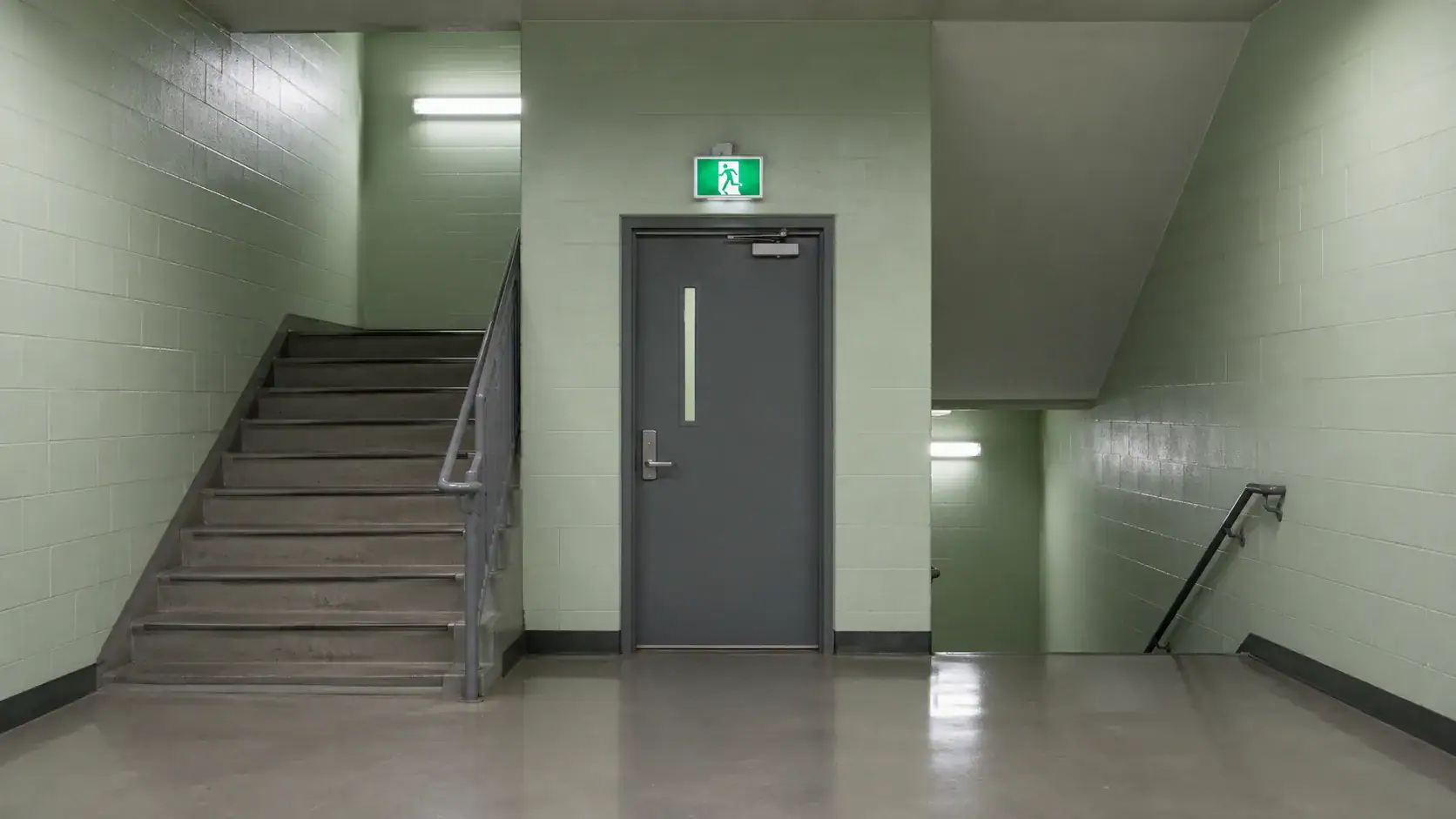 Institutionelles Treppenhaus mit Notausgangsschild — Behördenarchitektur im Strafverfahren.