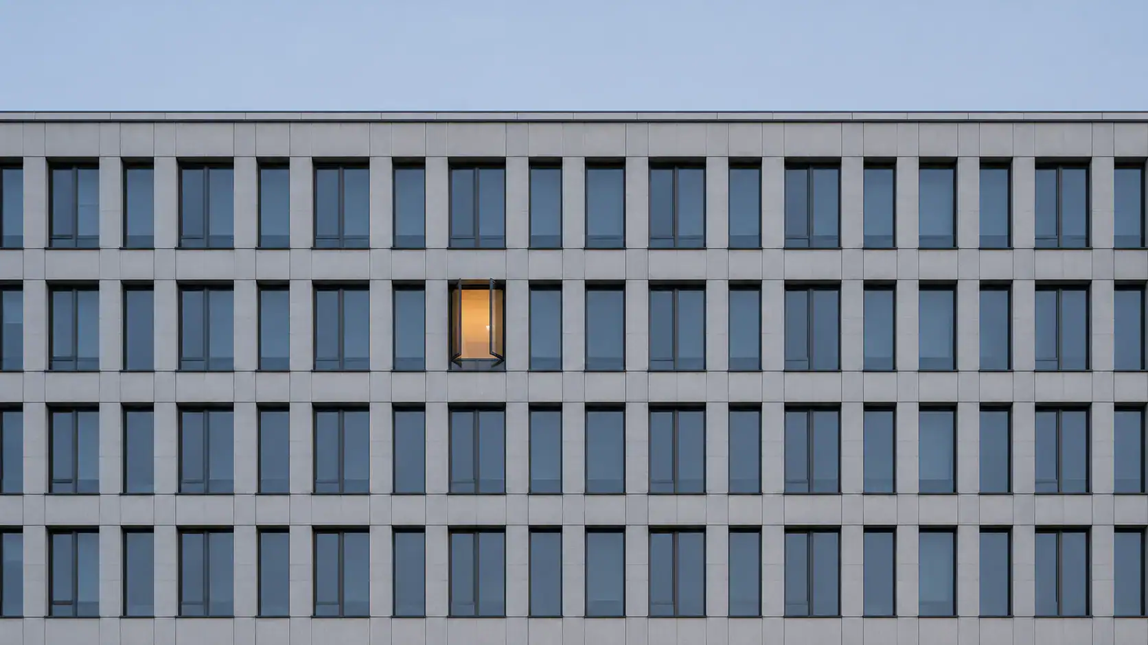 Bürofassade mit einem einzigen beleuchteten Fenster — Symbol für verborgene Ausforschung und den China-Wissenstransfer unter § 99 StGB