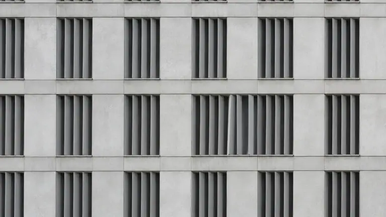 Betonfassade mit strengem Raster aus Lamellenfenstern, eine Lamelle steht verdreht — Symbolbild zur Steuerhehlerei mit unversteuerten E-Zigaretten (Symbolbild, KI-generiert)
