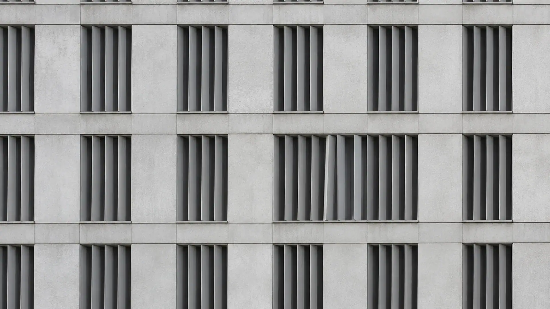 Betonfassade mit strengem Raster aus Lamellenfenstern, eine Lamelle steht verdreht — Symbolbild zur Steuerhehlerei mit unversteuerten E-Zigaretten (Symbolbild, KI-generiert)