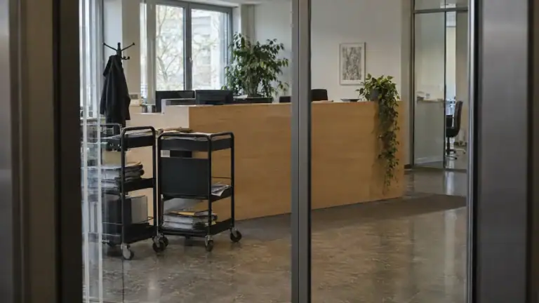 Empfang einer Prüfungsgesellschaft durch die Glastür gesehen, zwei Aktentrolleys am Tresen (Symbolbild, KI-generiert)