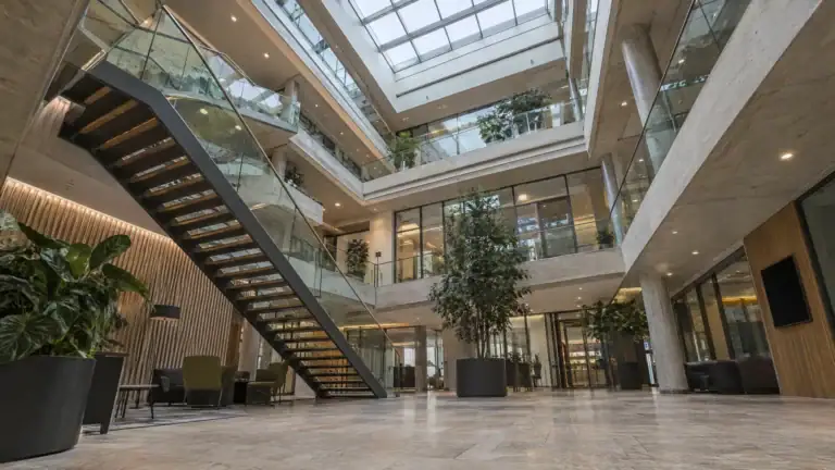 Atrium einer Unternehmenszentrale mit Glasbrüstungen, Galerien und Treppe unter Oberlicht (Symbolbild, KI-generiert)