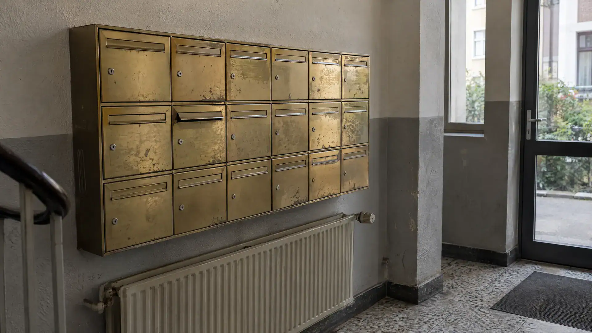 Briefkastenanlage im Eingang eines schlichten Bürohauses mit vielen leeren Namensschildern (Symbolbild, KI-generiert)