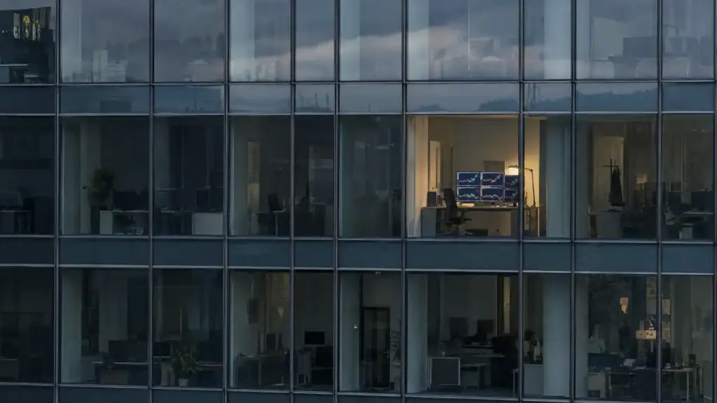 Dunkle Glasfassade eines Bürohochhauses, ein erleuchteter Raum mit mehreren Bildschirmen