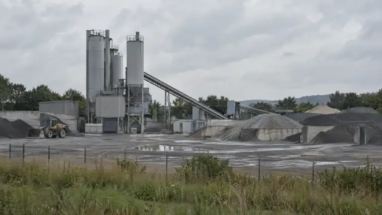 Asphaltmischanlage am Stadtrand mit Silos, Förderband und Splitthalden (Symbolbild, KI-generiert)
