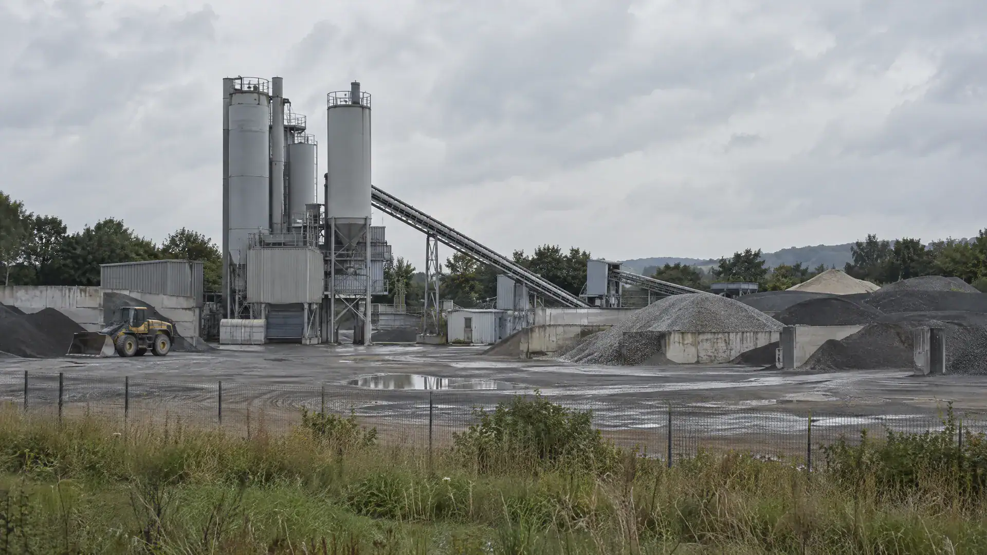 Asphaltmischanlage am Stadtrand mit Silos, Förderband und Splitthalden (Symbolbild, KI-generiert)