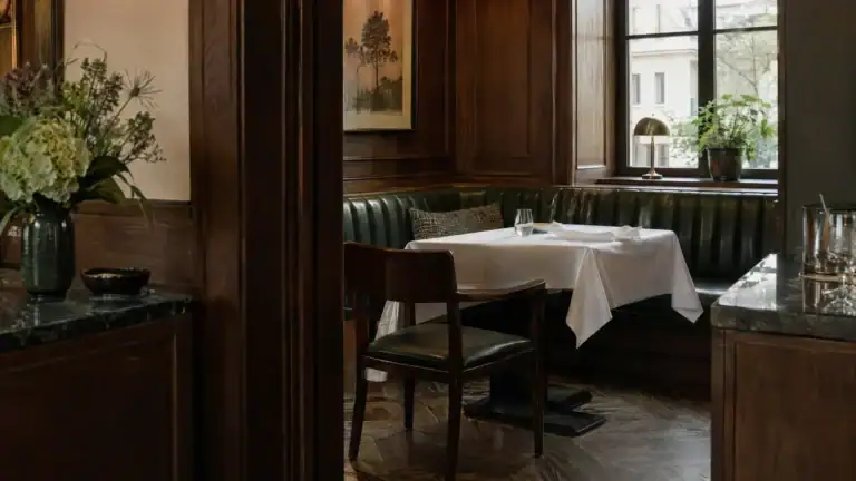 Separee eines Restaurants mit gedecktem Tisch, grüner Lederbank und dunkler Holzvertäfelung (Symbolbild, KI-generiert)