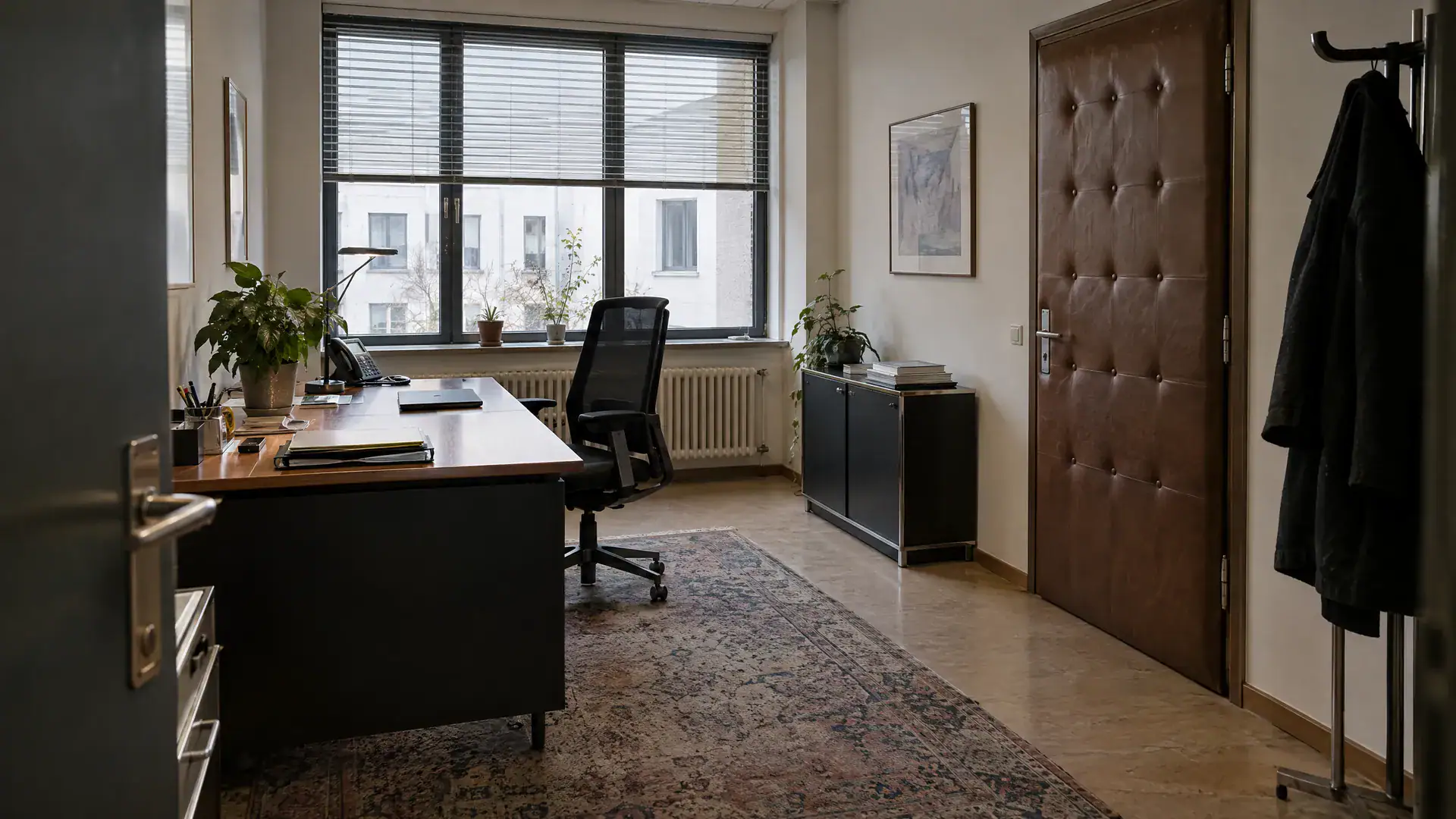 Vorzimmer eines Vorstands mit Schreibtisch, zugeklapptem Laptop und gepolsterter Tür (Symbolbild, KI-generiert)