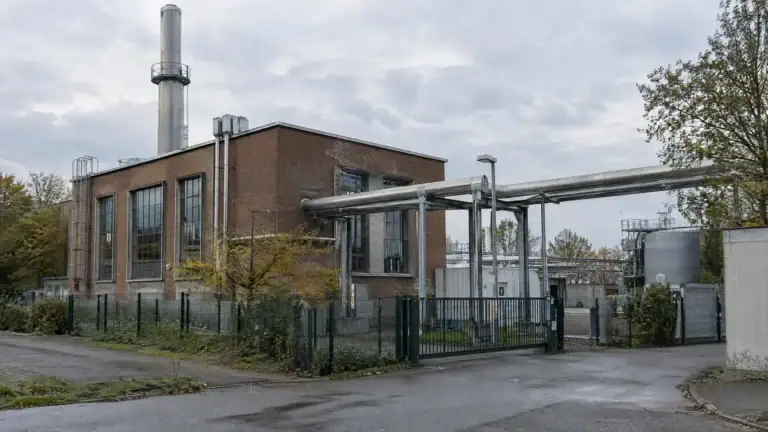 Kleines städtisches Heizkraftwerk mit Backsteinbau, Schornstein und Fernwärmeleitungen (Symbolbild, KI-generiert)